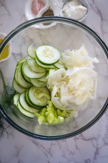 Ingredients for cucumber salad with fennel in a glass bowl.