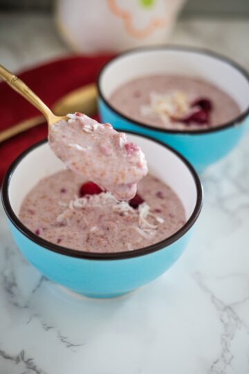 Two bowls of raspberry porridge with a spoon in them.
