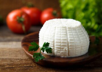 Cottage cheese on a wooden plate with tomatoes and parsley.