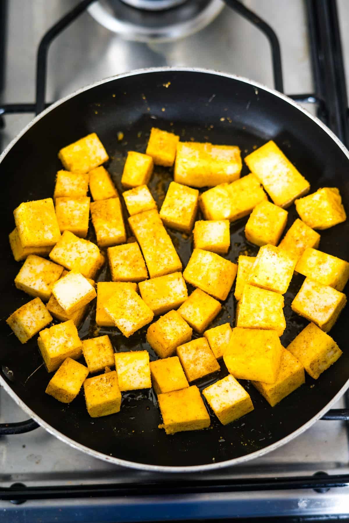 Fried tofu in a frying pan on a stove.