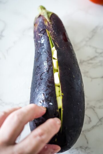 A person preparing Baigan Choka by cutting an eggplant with a knife.