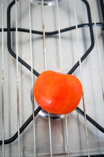 A red tomato sitting on a metal rack.