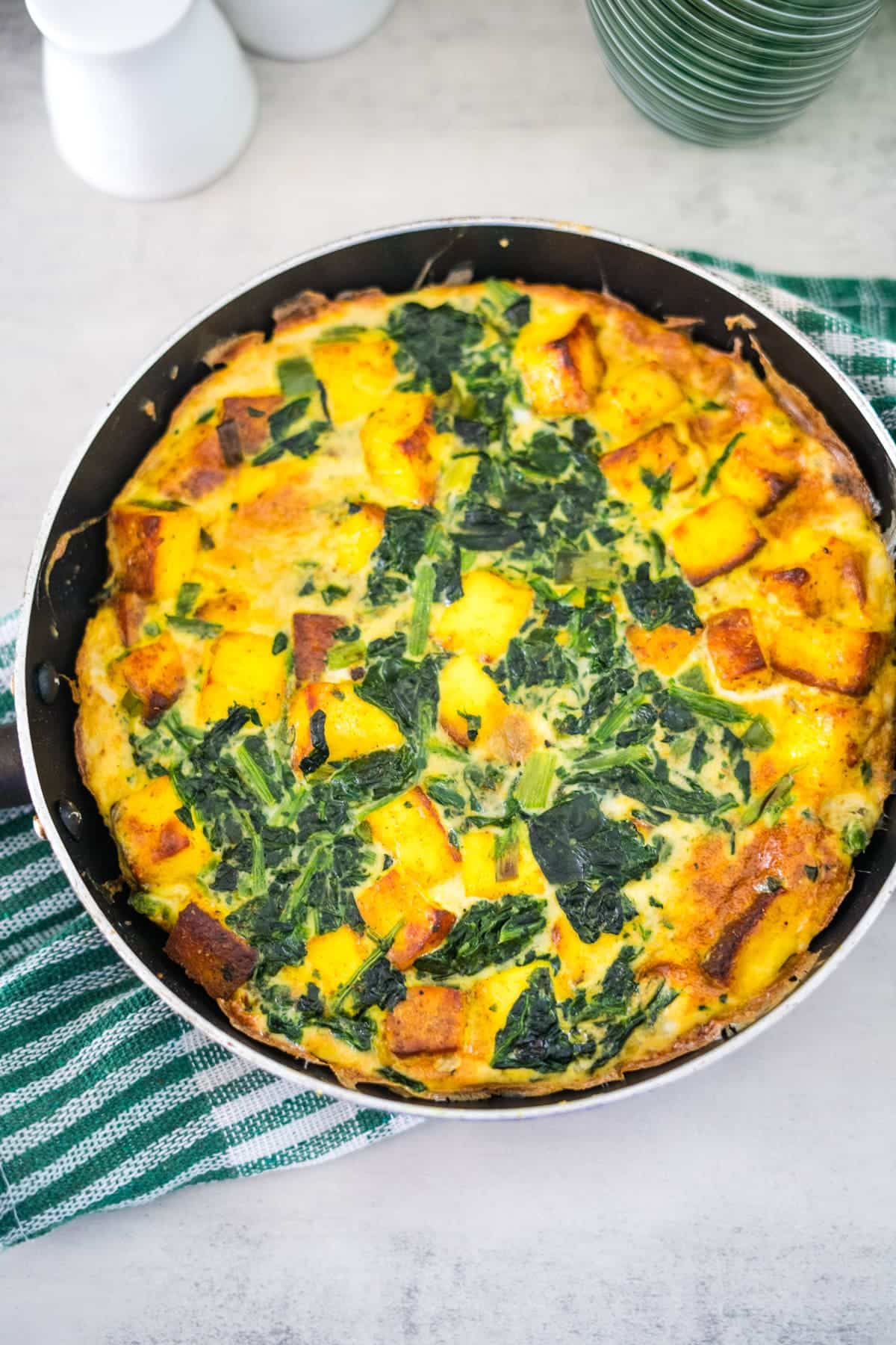A quiche with spinach and potatoes in a skillet.